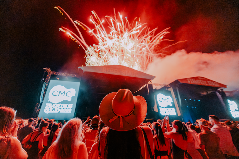 Country music fan in cowboy hat watching stage fireworks display at night during the CMC Rocks QLD 2026 festival at Willowbank Raceway in Queensland.